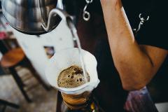 Coffeeholic Tour in Medellin A person is pouring hot water from a stainless steel kettle into a paper filter with ground coffee in a pour-over dripper.