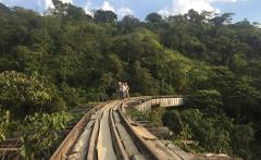 Three people stand on an old railway track, surrounded by lush green vegetation on a hillside.