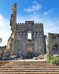Tur privat de 3 zile în Mogadiscio (istorie, cultură și coastă) The ruins of a grand stone building, possibly a church or castle, stand under a blue sky with rubble scattered at its base and a worn set of steps leading up to the entrance.