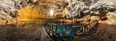 Panoramic view of a cenote featuring crystal clear turquoise water inside a cave, surrounded by wooden platforms and railings for visitors to enjoy the natural wonder.