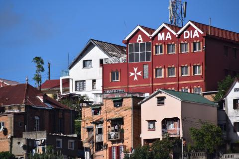 Free Daily Photography Walking Tour In Antananarivo's Historical City Center With Local Guide A vibrant cityscape featuring a mix of buildings, with a prominent red building displaying "A MA DIA" in large white letters, stands against a clear blue sky.