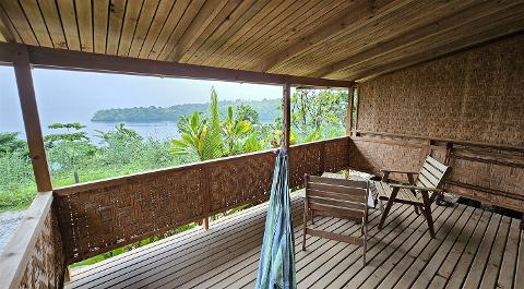 This is a covered wooden deck with chairs, a hammock, and a view of lush vegetation and a lake in the distance.