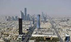 Here's a one-sentence description of the image:An aerial view captures the modern skyline of Riyadh, Saudi Arabia, with skyscrapers rising above a sprawling urban landscape under a hazy sky.
