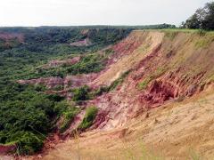 A dramatic landscape of a steep, eroded cliff face with reddish-pink rock layers and lush green vegetation at its base.