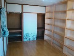 A room features a sliding door with a scenic painting, a hanging garment, built-in closets, and a tall bookshelf.