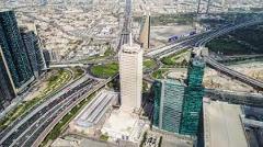 An aerial view captures the bustling cityscape of Dubai, featuring skyscrapers, intricate highway systems, and lush greenery, showcasing the city's modern infrastructure and urban development.