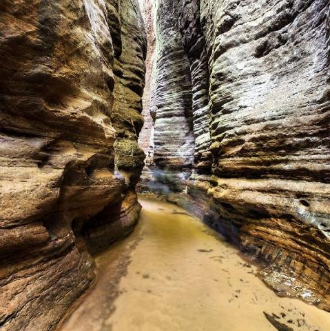 A narrow slot canyon with water flowing through, showcasing layered rock formations and a sense of depth.