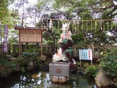 This image captures a tranquil scene in a Japanese garden, featuring a white dragon statue beside a pond, a wooden sign with Japanese text, and a rope strung with paper decorations, surrounded by lush greenery.
