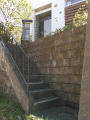 A stone staircase with a metal railing leads up to the entrance of a modern house with a wooden-slatted window.