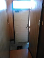 Two dark slippers sit on a gray mat in front of a white door with horizontal panels.