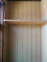 A simple wooden shelf is mounted on a wall paneled with vertical wood planks in a room with natural light.