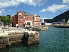 A sunny day at a harbor with a brick building near the water and a mountain in the background.