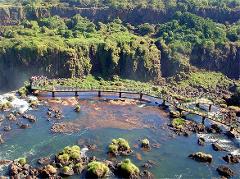 A scenic view of a long bridge with tourists spanning across a waterfall with lush green vegetation and rock formations.