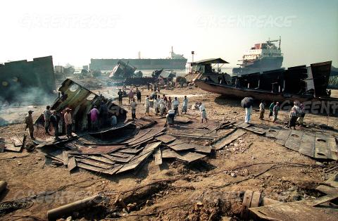 Workers dismantling ships at a shipbreaking yard, surrounded by debris and large vessels.