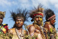 A group of people from Papua New Guinea are wearing traditional clothing, including headdresses, beads, and face paint, against a blue sky.