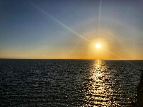 The image shows a serene sunset over the ocean with the sun reflecting golden light on the water, creating a peaceful and warm atmosphere.