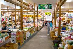 This is an indoor marketplace in Japan with vendors selling fruits, vegetables, and seafood to customers walking through the aisle.