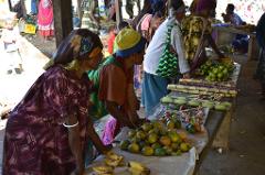 A bustling open-air market scene with local vendors selling fresh produce, including oranges, bananas, and sugar cane, showcasing the vibrant culture of Papua New Guinea.