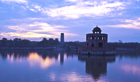 A tranquil scene of a historic structure in a lake reflects the colorful twilight sky.
