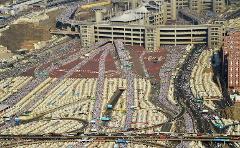 An aerial shot shows a sprawling landscape filled with white tents, roads teeming with buses, and massive crowds of people, likely during a pilgrimage.