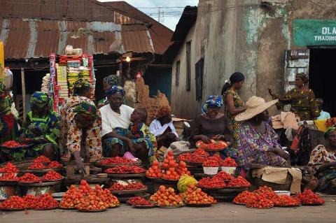 A vibrant street market scene in Africa with women selling vibrant red tomatoes and peppers.