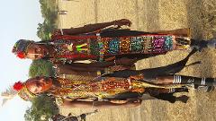 Two elaborately adorned men in ceremonial attire stand side-by-side in a grassy field, their faces painted with traditional markings, showcasing vibrant colors and intricate beadwork.