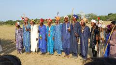 A group of men in traditional costumes and face paint stand in a line in an outdoor setting.