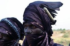 A close-up shows a Tuareg man in a blue turban and face veil, with a decorative cylinder attached to his headwear, during the Bianou Festival in Niger.