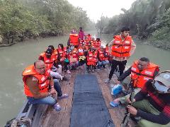 A group of people, wearing orange life vests, are traveling on a boat through a waterway lined with lush greenery.
