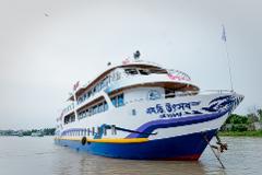 A multi-decked river cruise ship, painted white and blue, is anchored in a body of water against a cloudy sky, with greenery visible on the distant shoreline.