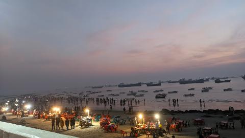 A beach in Bangladesh at dusk, with numerous ships at anchor and people dining at seaside food stalls.