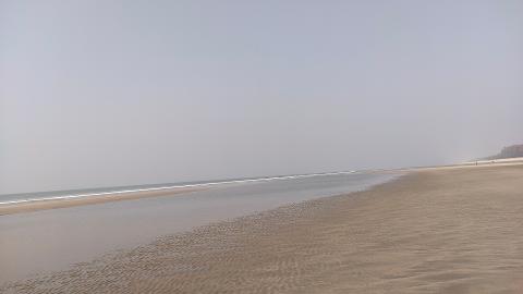 A vast, sandy beach stretches towards a distant tree-lined coast under a pale sky.