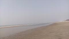 A vast, sandy beach stretches towards a distant tree-lined coast under a pale sky.