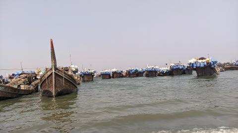 A fleet of fishing boats laden with blue and white containers is anchored in the water under a clear sky.