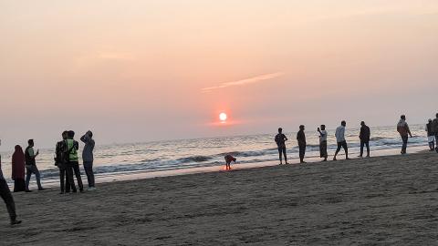 A serene sunset over the ocean at Cox's Bazar beach, with a line of people enjoying the view and the gentle waves.