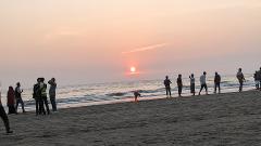 A serene sunset over the ocean at Cox's Bazar beach, with a line of people enjoying the view and the gentle waves.