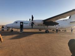 A turboprop plane belonging to Niger Airways is parked on the tarmac with passengers disembarking or preparing to board via the stairs.