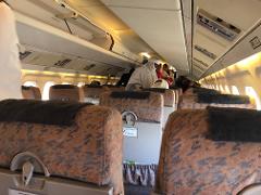 The interior of an NTT Express Plane shows rows of seats with passengers boarding or deplaning, luggage compartments above, and overhead lights.