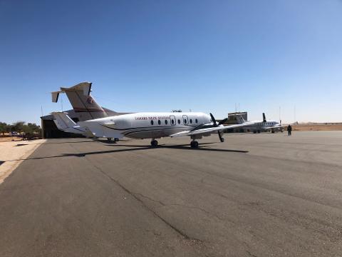 Several airplanes, including a Beechcraft 1900D with "TAMARA NIGER AVIATION" written on it, are parked on a tarmac under a clear blue sky.
