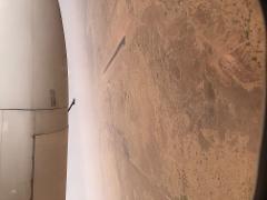 An aerial view from an airplane window shows an arid landscape with an airport runway and buildings, and a part of the plane's engine.