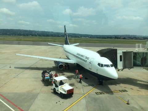 A Canadian Airways Congo airplane is parked at an airport gate, with luggage being unloaded by ground staff.