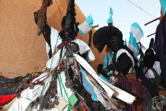 The image shows elaborately costumed men, likely participating in the Bianou & Gerewol Festival, adorned with vibrant colors, tassels, flags, and leather embellishments, engaging in a ceremonial performance.