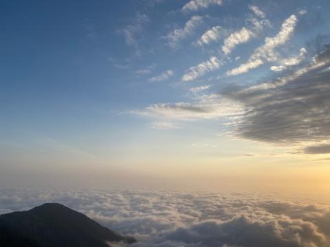 A breathtaking view from above, featuring a mountain peak emerging from a sea of clouds under a vibrant sky.