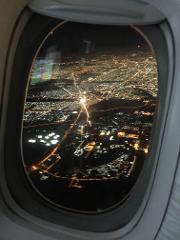 An airplane window view captures a sprawling city at night, illuminated by a network of twinkling lights and roads.