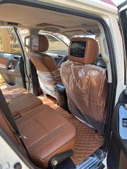 The interior of a car with brown leather seats is shown, protected with plastic covers.  A screen is on the back of one of the front seats, and a patterned brown floor mat is visible.