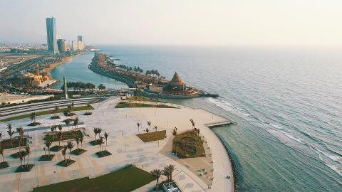 An aerial view captures a coastal scene with modern architecture and palm-lined esplanades along the Red Sea.