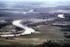 An aerial shot of a meandering river winding through a flat, marshy landscape dotted with trees.