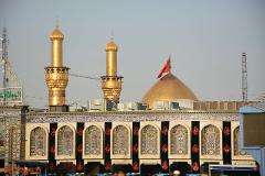 A mosque with golden minarets and a dome, adorned with black banners and Arabic calligraphy.
