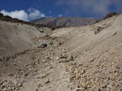 A rugged, rocky landscape on Mount Kilimanjaro, with a view of the mountain peak against a blue sky with scattered clouds.