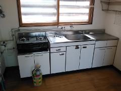 A utilitarian kitchen area with a gas stove, sink, and cabinets is visible, with a small fire extinguisher in the foreground.